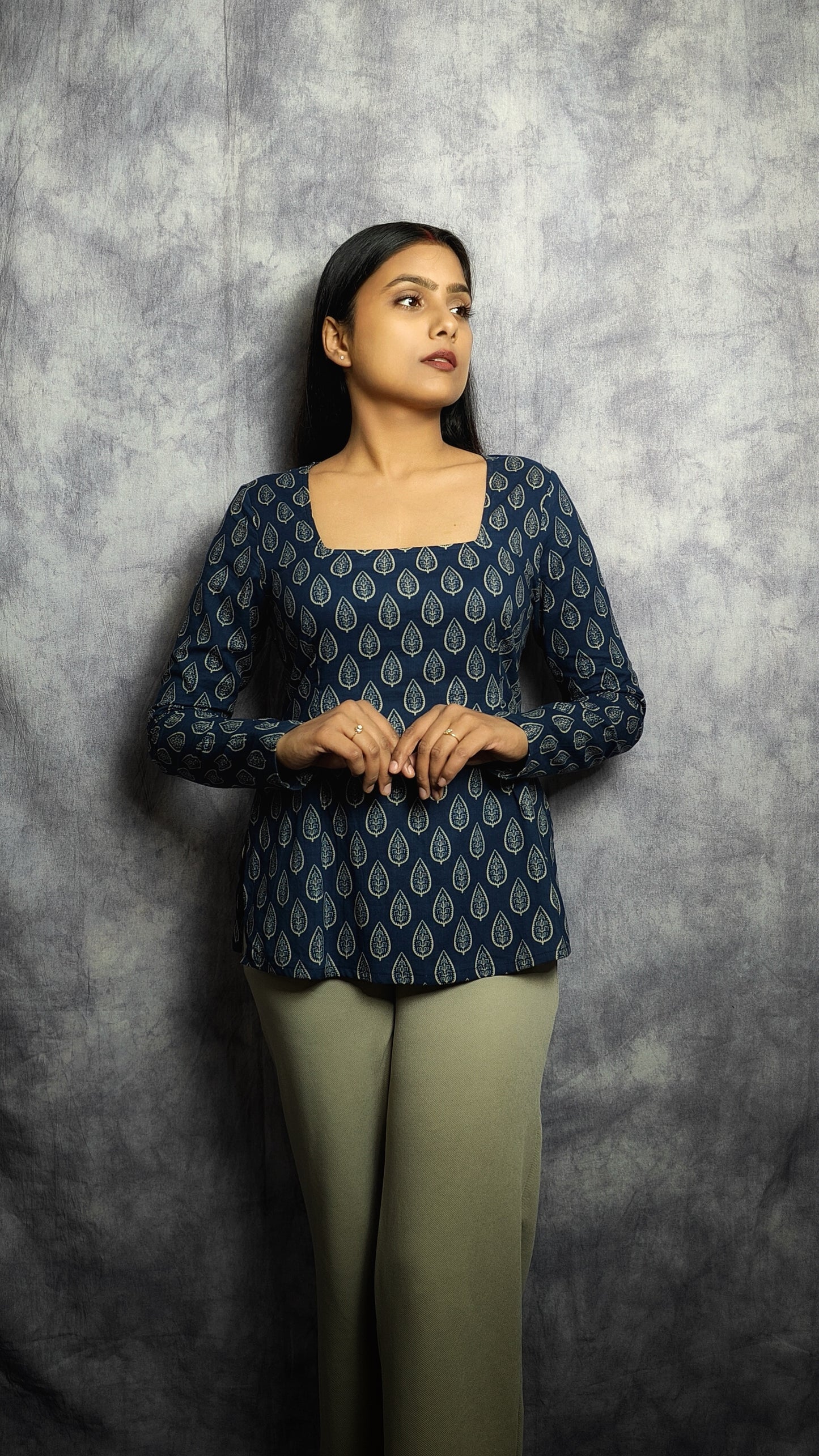 Woman wearing a dark blue patterned top and green pants against a gray background