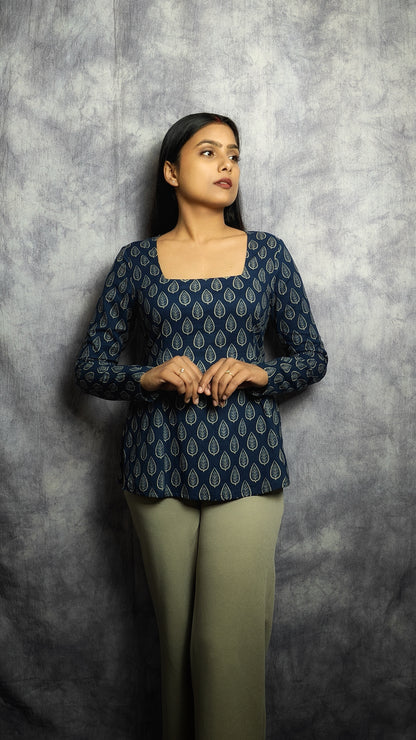 Woman wearing a dark blue patterned top and green pants against a gray background
